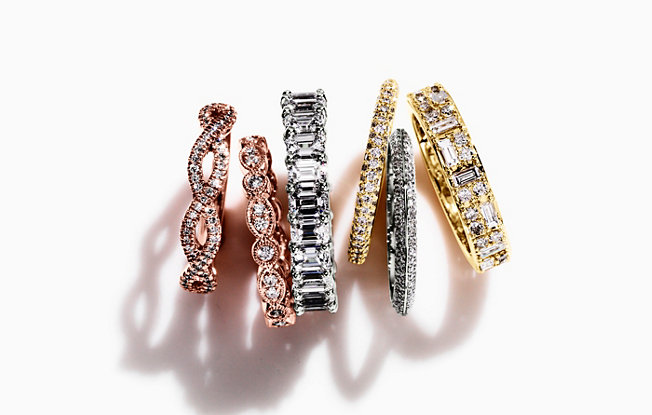 Several diamond wedding bands in various metals and shapes on a white background