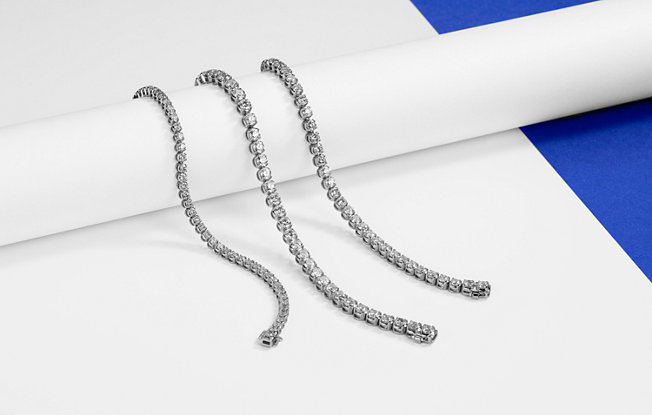 Three diamond tennis bracelets lay across a pole on a blue background