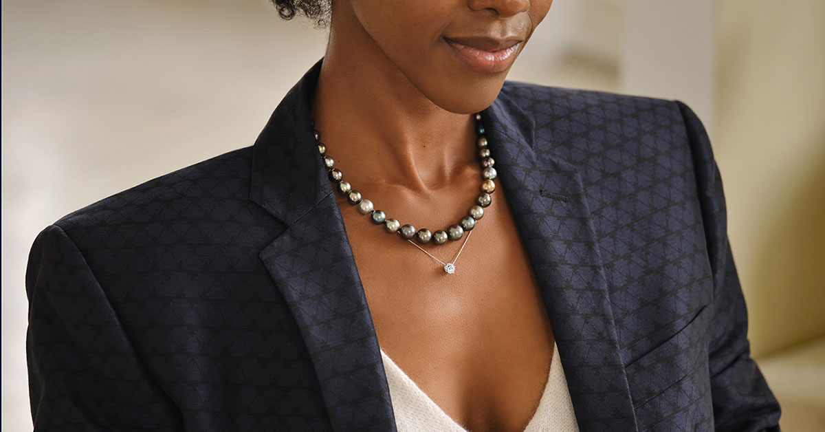 Close up of a woman’s décolleté area, she is wearing a pearl necklace and a custom diamond pendant. 