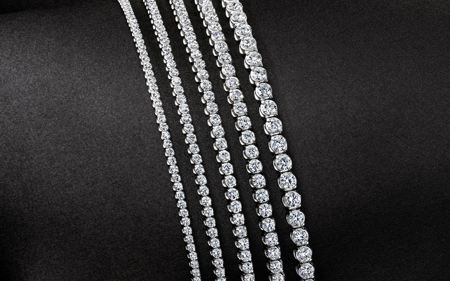 Five tennis bracelets of ascending carat sizes.