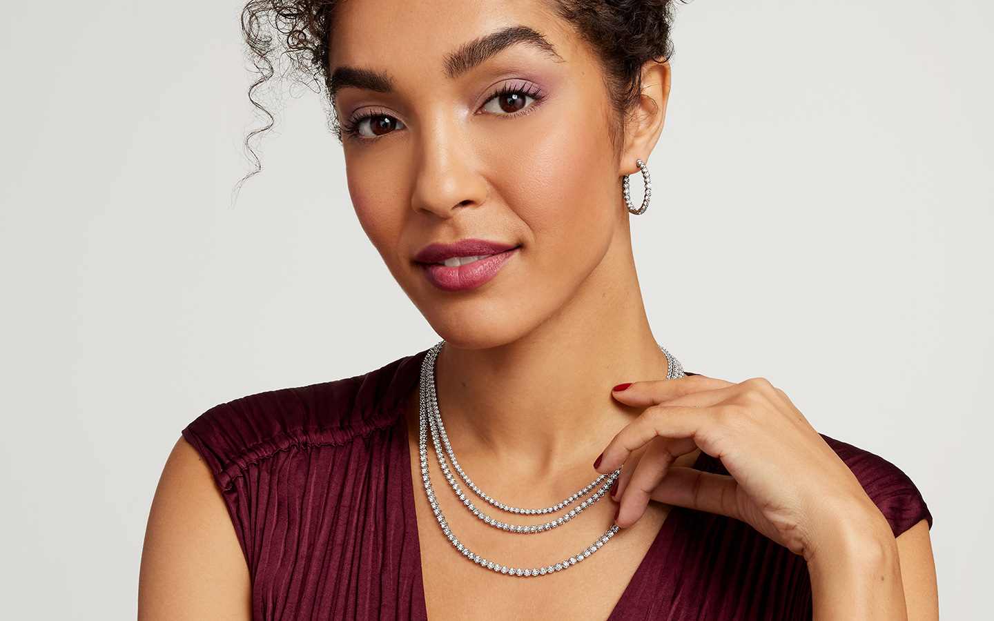 Woman wearing diamond birthstone necklaces and hoop earrings.