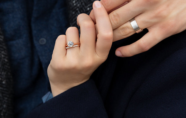 A man's hand wearing a white gold wedding band and a woman's hand wearing a yellow gold and diamond bridal set