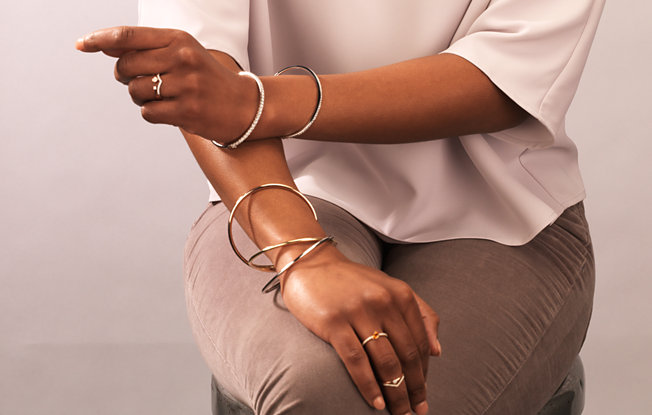 A woman sitting in a chair modeling several gold bracelets and rings