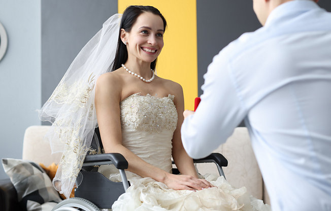 A man kneeling down to present a ring to his bride who is in a wheelchair