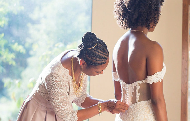 An older woman helps a younger woman put on her wedding dress