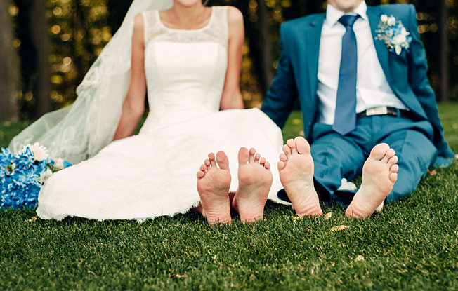 Bride and Groom sit barefoot on a green lawn