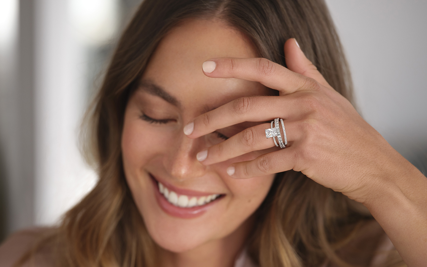 Photo of a smiling woman covering her face with her left hand, she is wearing a Blue Nile diamond wedding set.