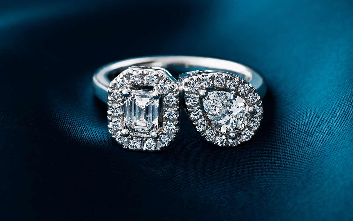 Two-stone engagement ring with pear and emerald diamonds and halos around each diamond in 14k white gold. 