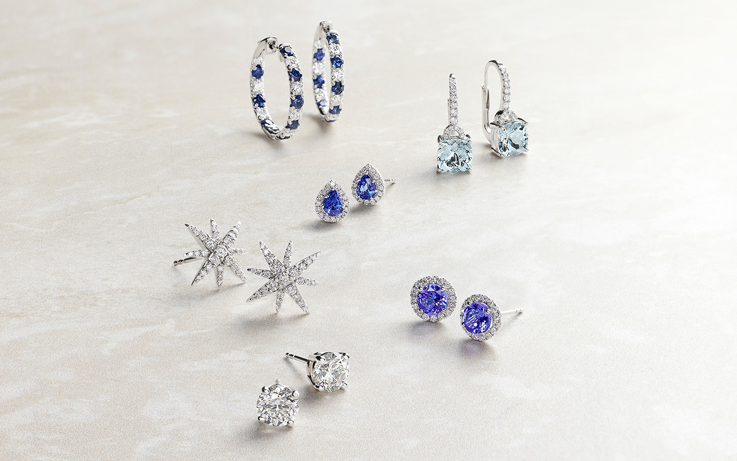 Pairs of sapphire, aquamarine, tourmaline and diamond earrings on a light background. 