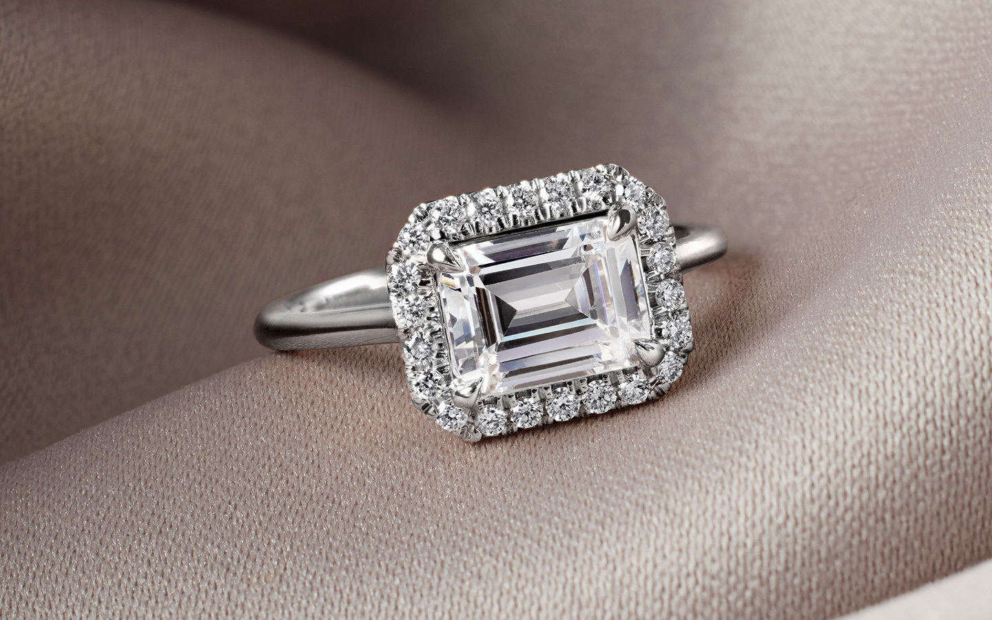 White gold and emerald east west engagement ring with a diamond halo.