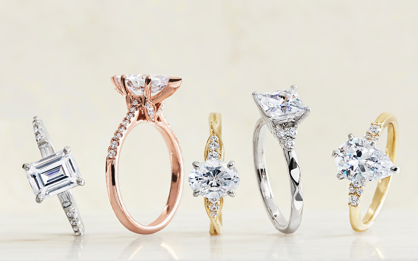 Five platinum, rose gold and white gold diamond engagement rings on a light background.