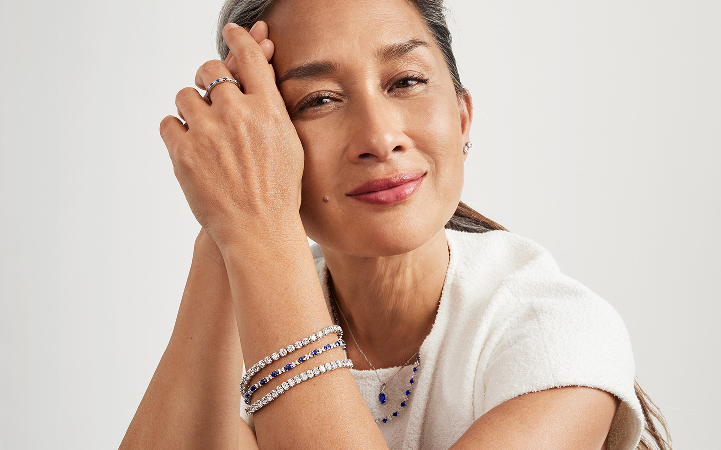 Portrait of a woman smiling softly, she is wearing gemstone jewelry.