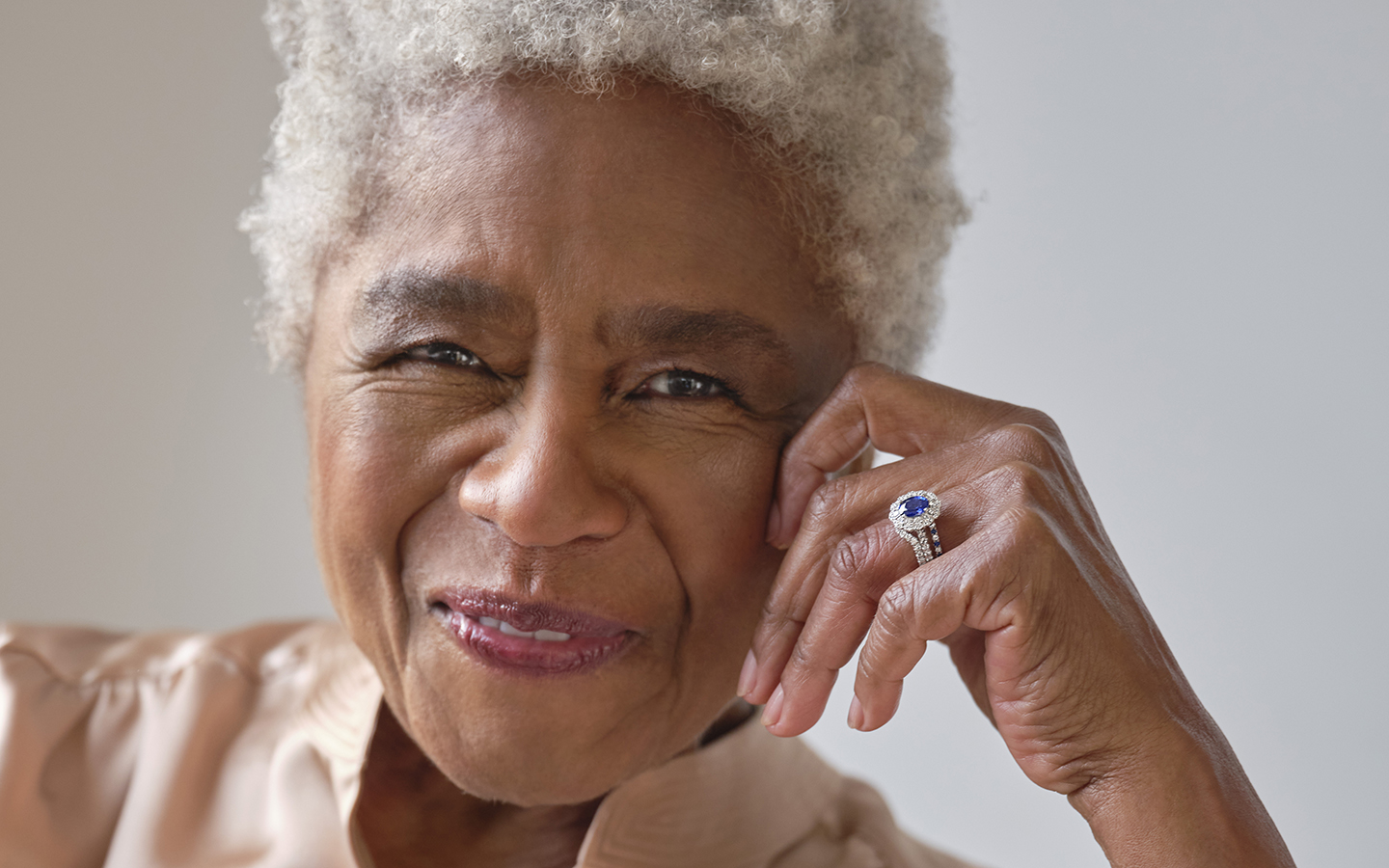 Older woman smiling as she wears a gemstone ring.