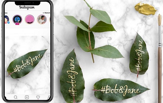 A phone, green leaves and a paintbrush on a marble background