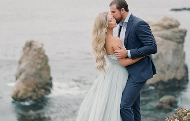 A woman in a blue dress embraces a man in a suit at the beach