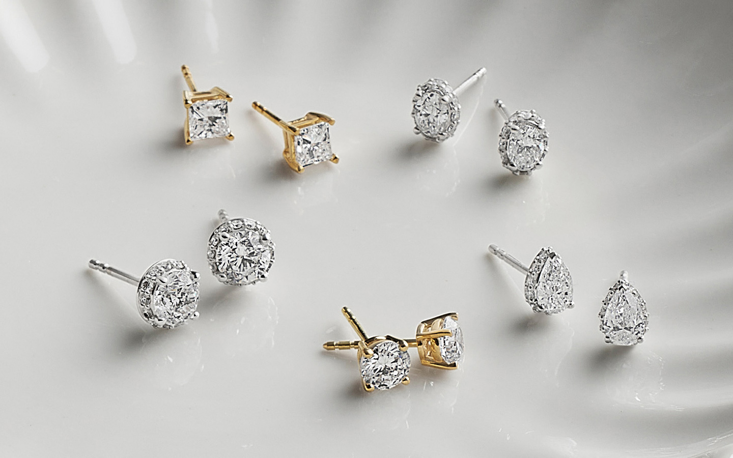 Five pairs of gold and diamond earrings on a light dish. 