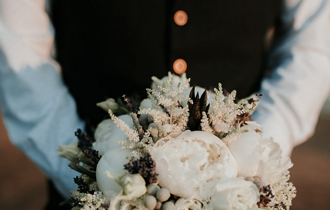 A man in a wedding suit holds a bouquet of flowers