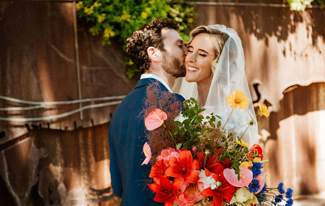 A man in a suit kissing a woman in a veil and wedding dress on the cheek