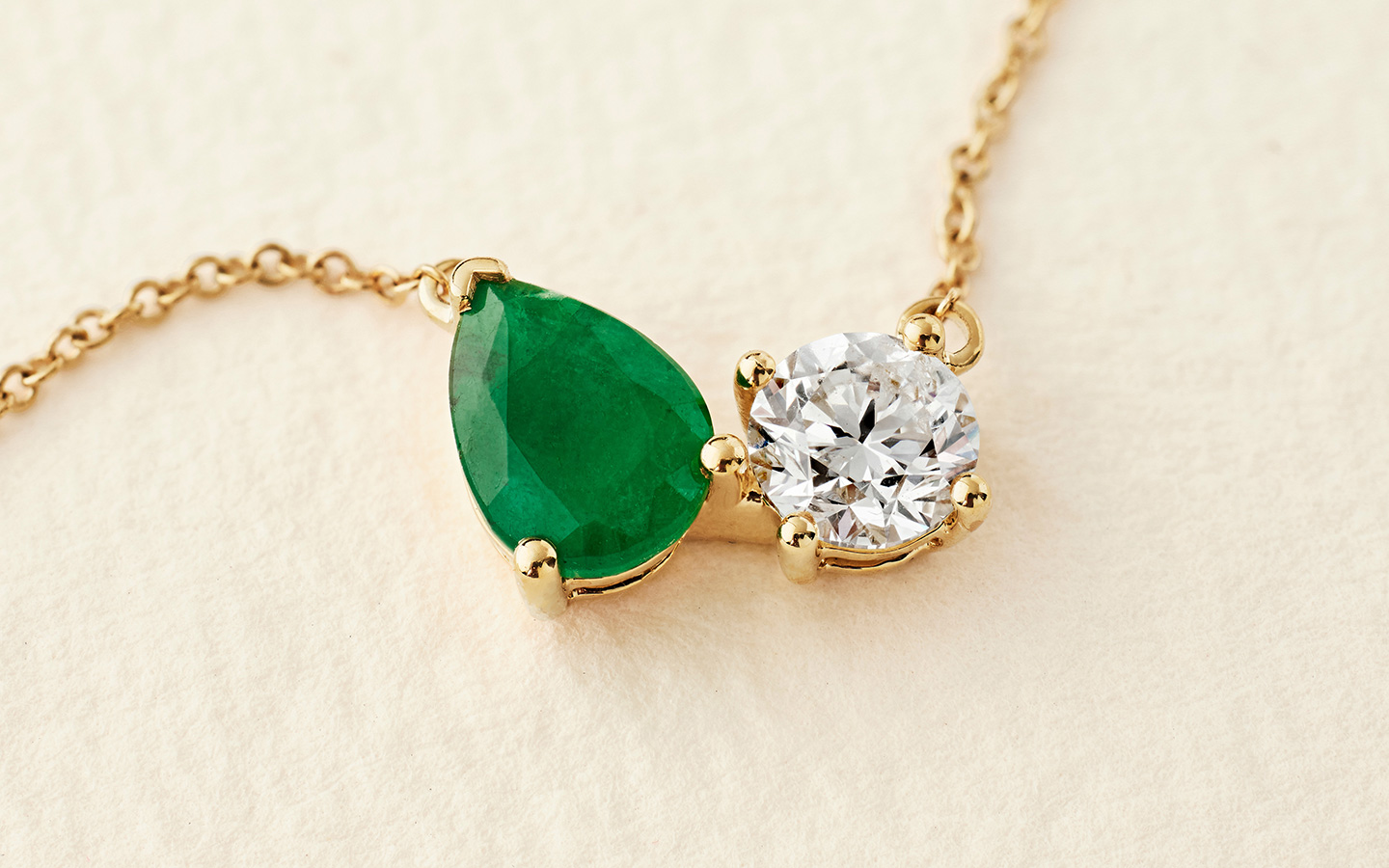 Close up of a dainty emerald and diamond necklace in yellow gold. 