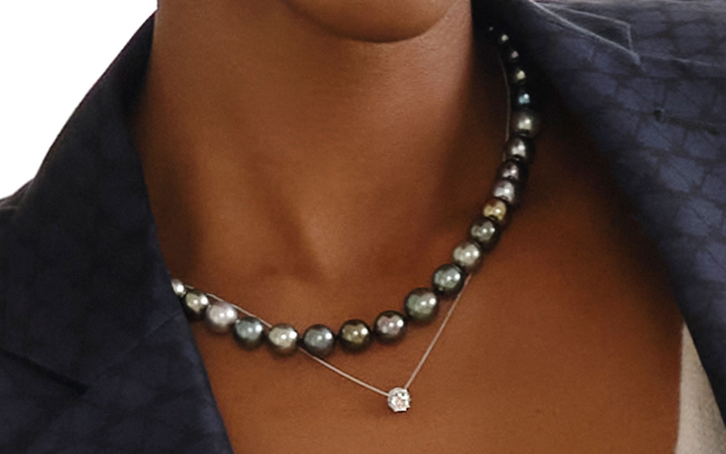 Close up of a woman’s necklaces, she is wearing a diamond pendant and a pearl necklace. 