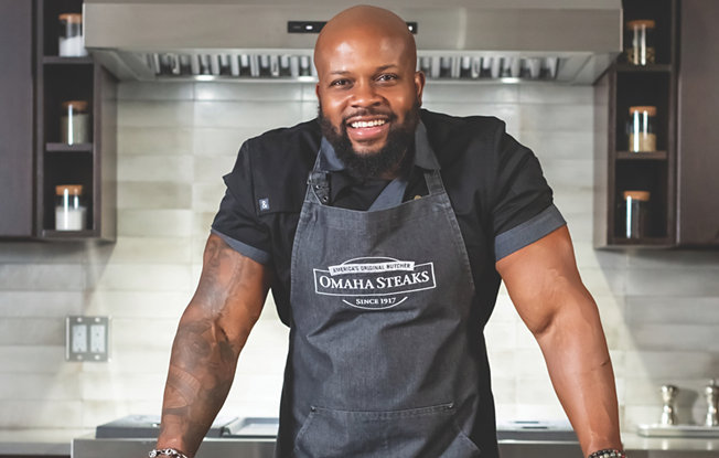 A man standing at a kitchen bench wearing an apron