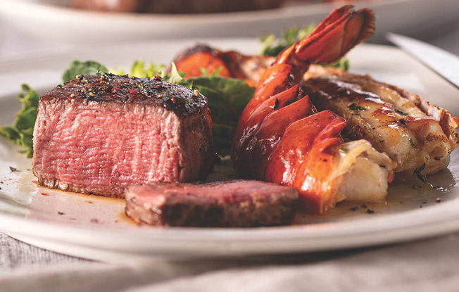 A piece of grilled steak and a lobster tail with veggies on a white plate
