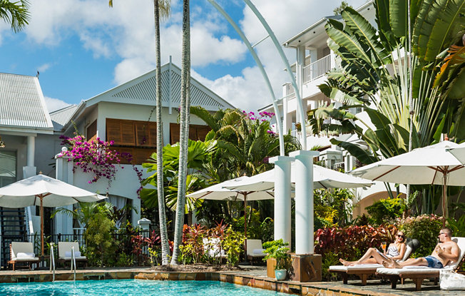 A couple sits on beach chairs in front of a pool at a tropical resort