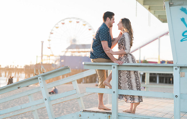 Man and woman on lifeguard tower gaze into each others eyes in front of Sata Monica Pier