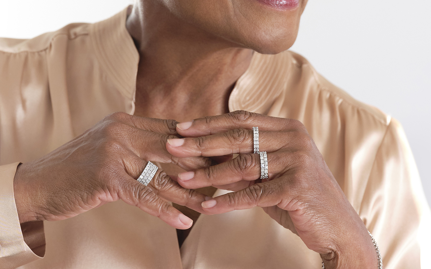 Photo of woman’s hands, she is wearing multiple diamond eternity ring stacks.