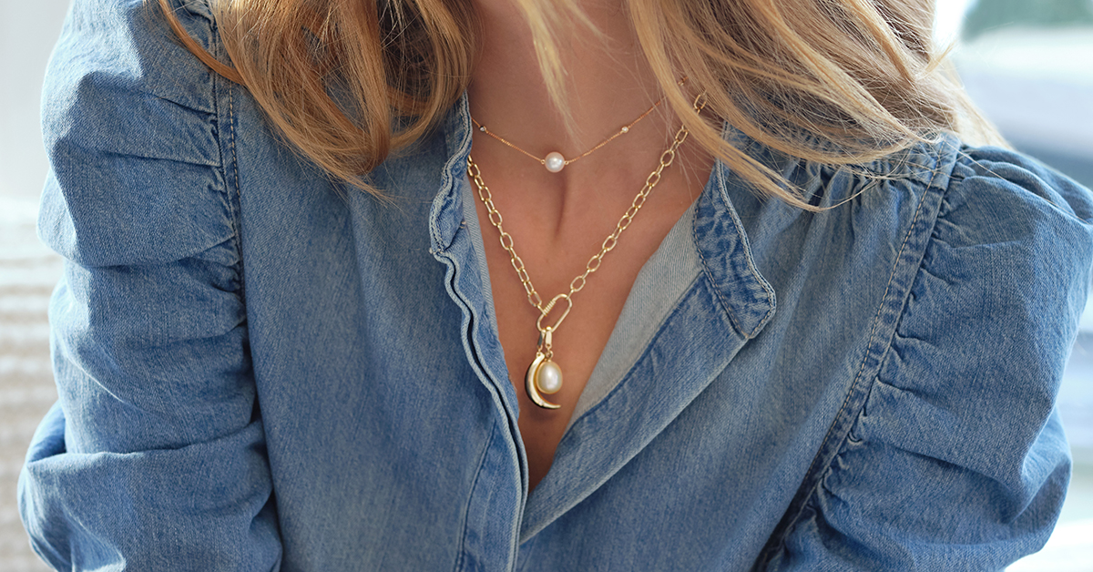 Photo of a woman’s 2 gold necklaces, she is wearing them alongside a denim top.  