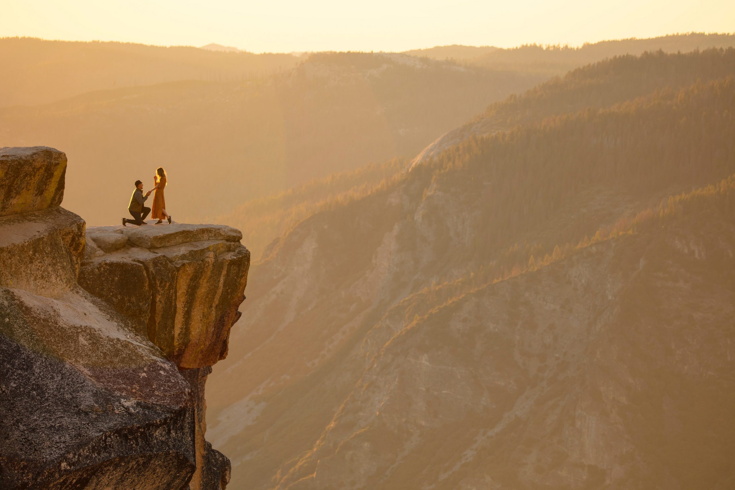 Photo from afar of a man proposing to his partner at a national park.