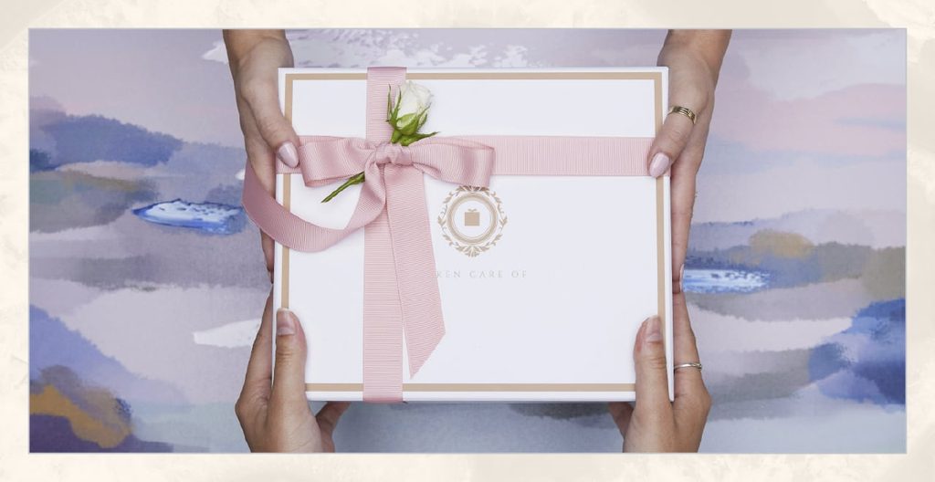 Hands passing a white box tied with a pink bow and white rose. 