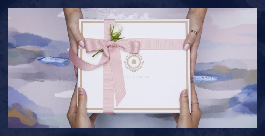 Hands passing a white box tied with a pink bow and white rose.