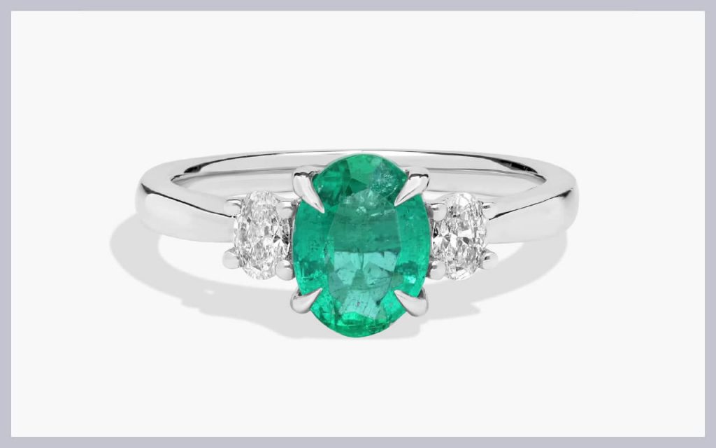 Oval emerald centered between two white side stones, offering rich color for non-traditional engagement ring stones