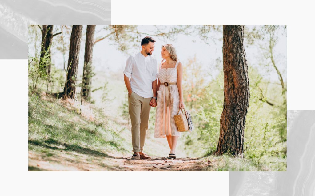 An engaged couple walking along a path in the woods, staring at each other.