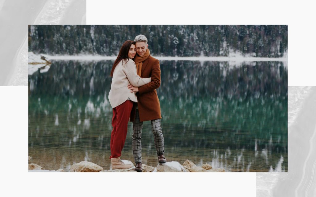 An engaged couple on a walking trail posing next to a lake at winter time. 