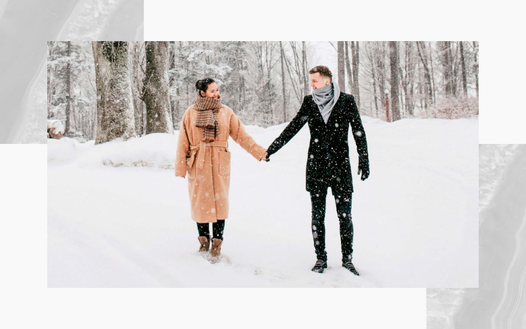 An engaged couple walking through the snow.