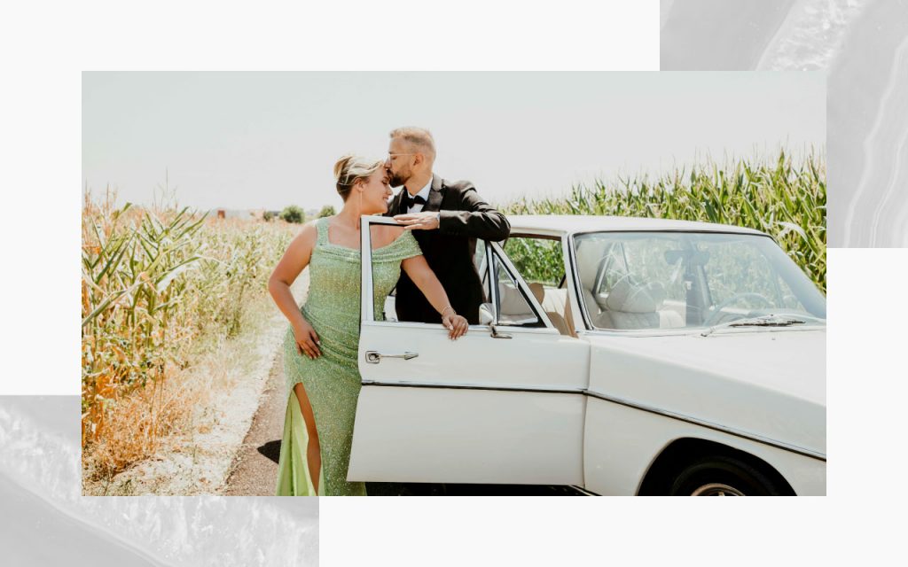 An engaged couple posing with a vintage vehicle. 