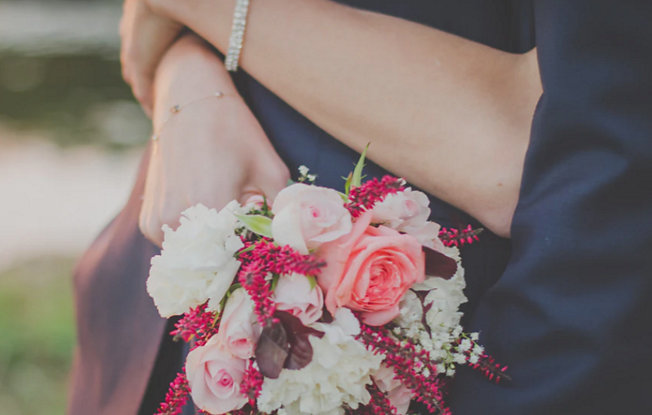 A woman wearing a diamond tennis bracelet has her arms around a man in a suit and is holding a bridal bouquet