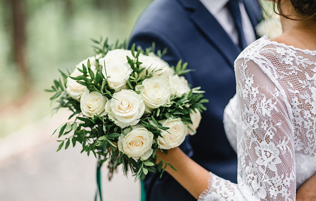 A woman in a wedding dress embraces a man in a suit while holding a bouquet of white flowers