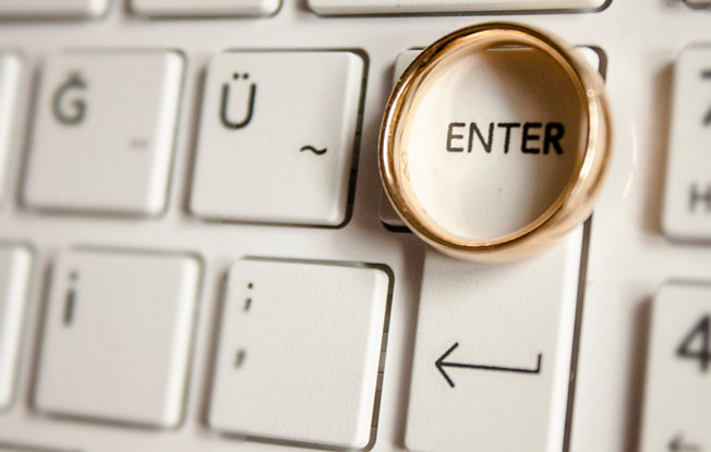 A plain gold wedding band sits on the keyboard of a computer