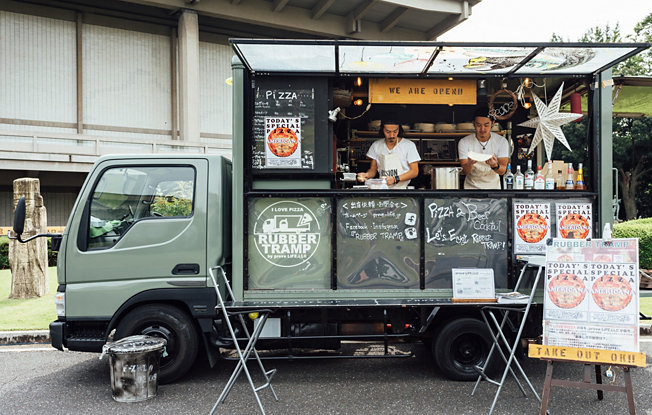 A green food truck selling pizzas sits on the street outside of a building