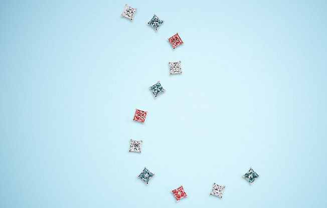 Eleven lightbox cushion cut lab grown diamonds in white pink and blue laid out on a blue background
