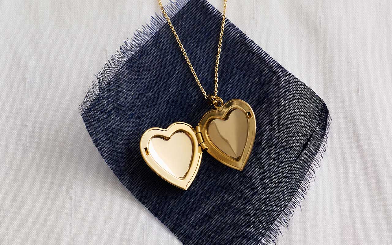 Gold heart locket necklace layered on fabric from the Blue Nile Modern Vintage Romance Collection