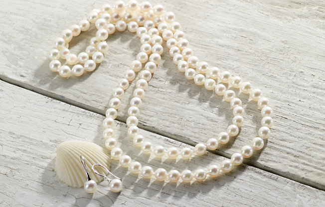 Pearl necklace and earrings displayed on weathered wood by sea-shell