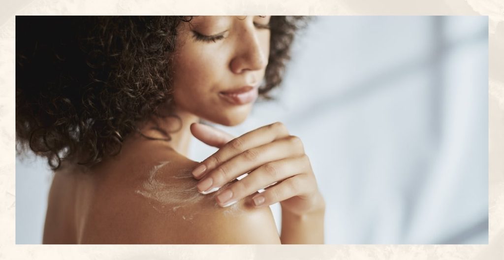 A woman applies body lotion to her shoulder.