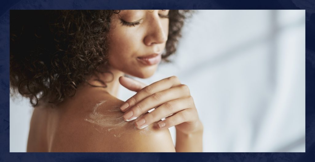 A woman applies body lotion to her shoulder.