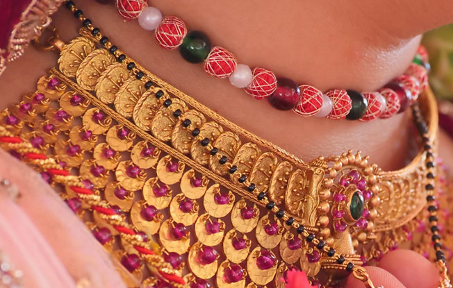 A close up of a traditional yellow gold Indian choker with pink beads